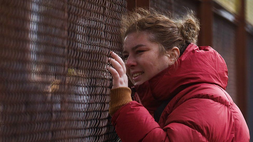 A woman leans against a fence as people from Ukraine arrive at the main railway station in Przemysl, Poland