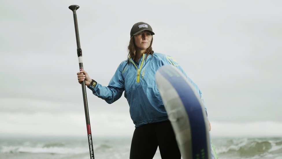 Sian Sykes with a paddleboard stood in the sea
