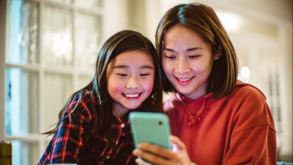 A mother and daughter smiling as they look at a phone screen