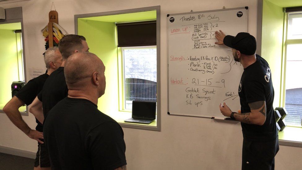 personal trainer pointing at instructions on a whiteboard