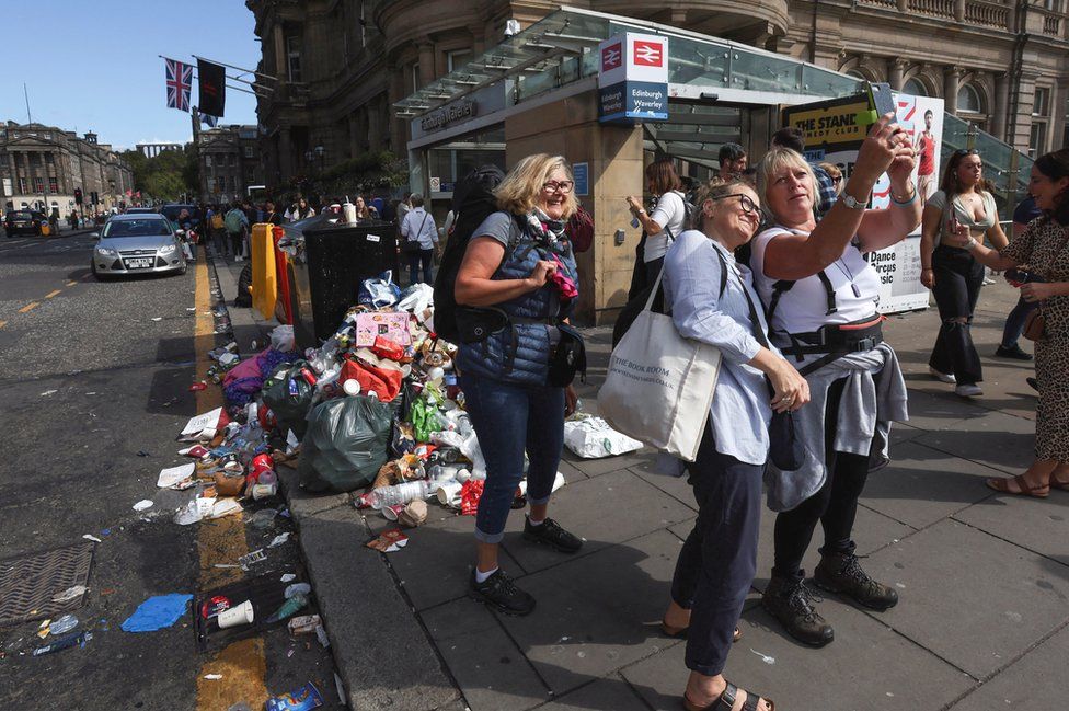 Tourists pose for pictures beside overflowing bins in Edinburgh