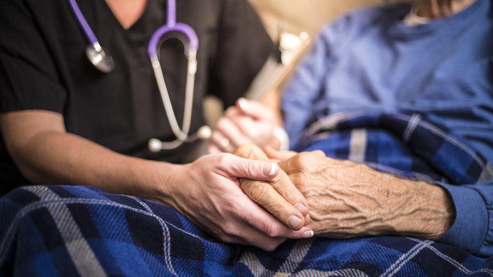 An elderly patient has their hand held by a carer