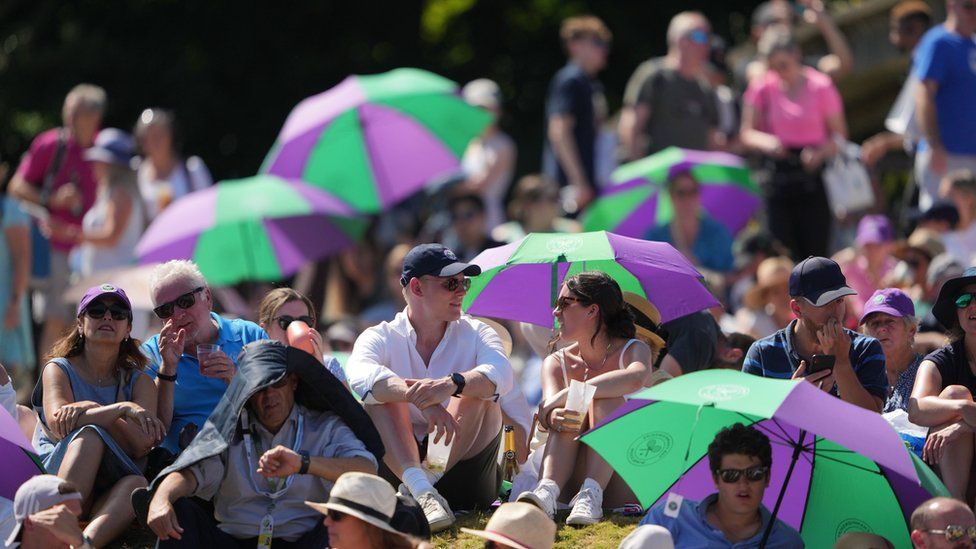 Spectators shield from the sun on day twelve of the 2022 Wimbledon Championships