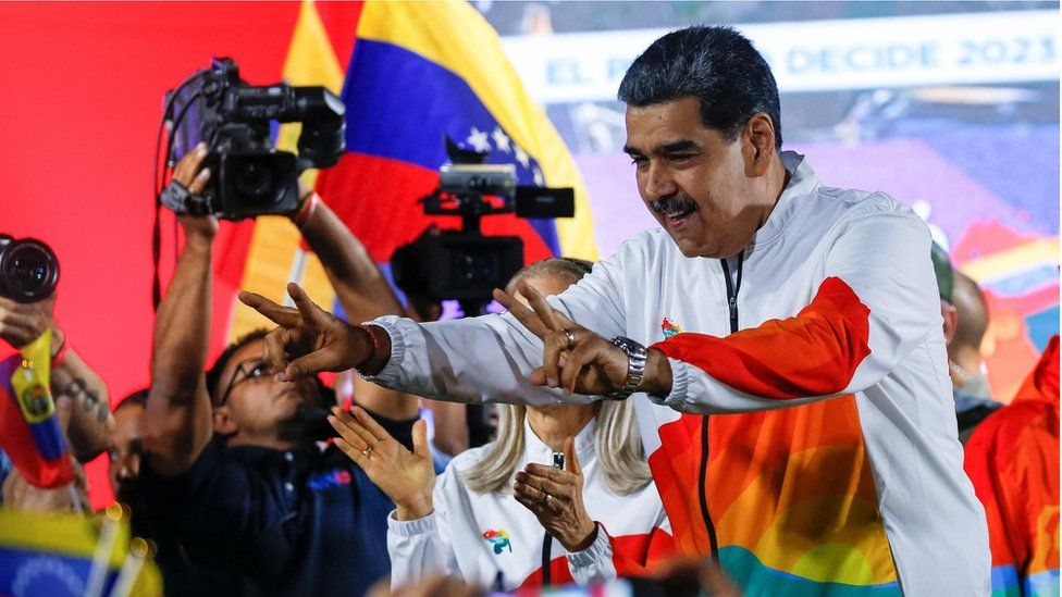 Nicolás Maduro in a white and rainbow hoodie with hands raised