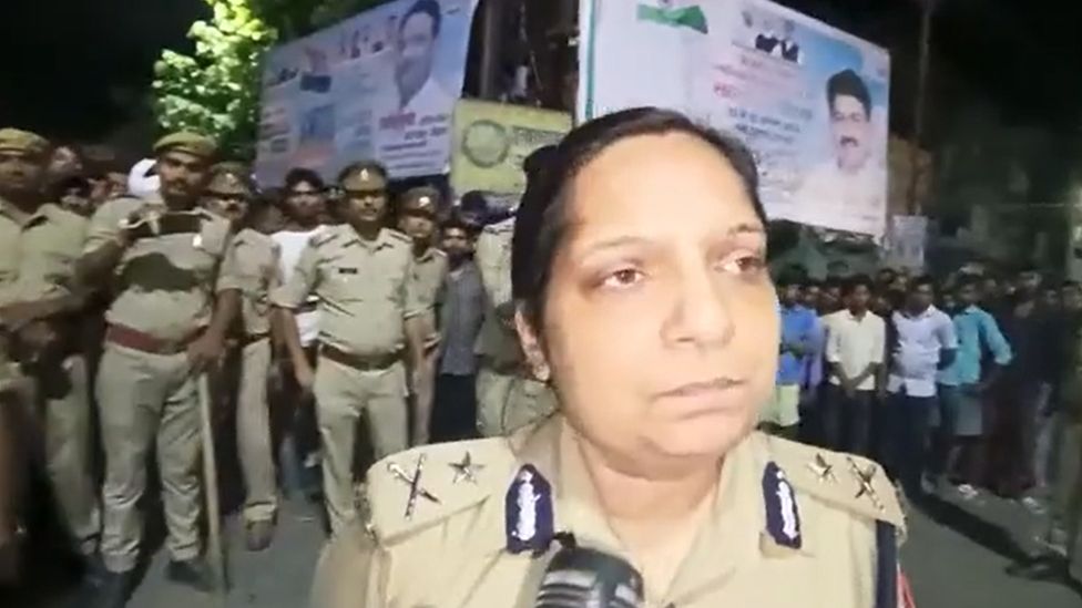 An Uttar Pradesh policewoman speaks to reporters in front of a crowd of police and locals in the district where the girls' bodies were found