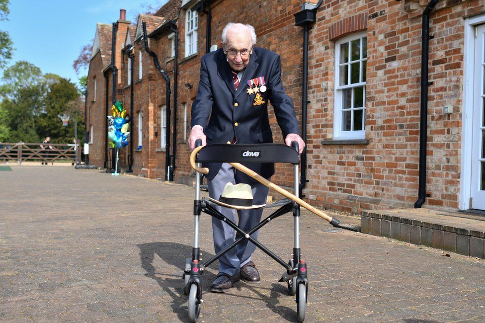 Captain Sir Tom Moore walks alongside his house whilst holding on to a walking frame