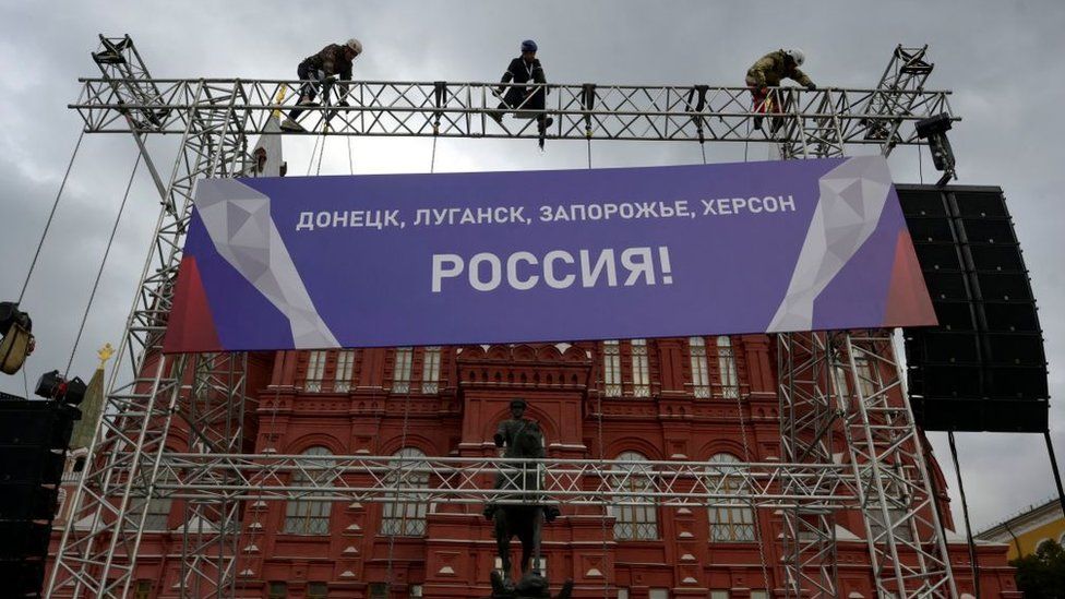 Workers fix a banner reading "Donetsk, Lugansk, Zaporizhzhia, Kherson - Russia!" on top of a construction installed in front of the State Historical Museum outside Red Square in central Moscow on September 29, 2022