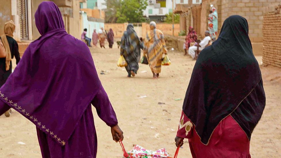 Women walk down a street carrying bags in Greater Khartoum, Sudan - May 2023