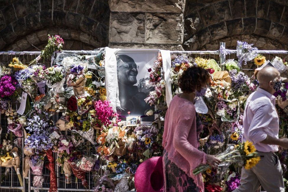 People bring flowers to leave in tribute to the late Archbishop Desmond Tutu