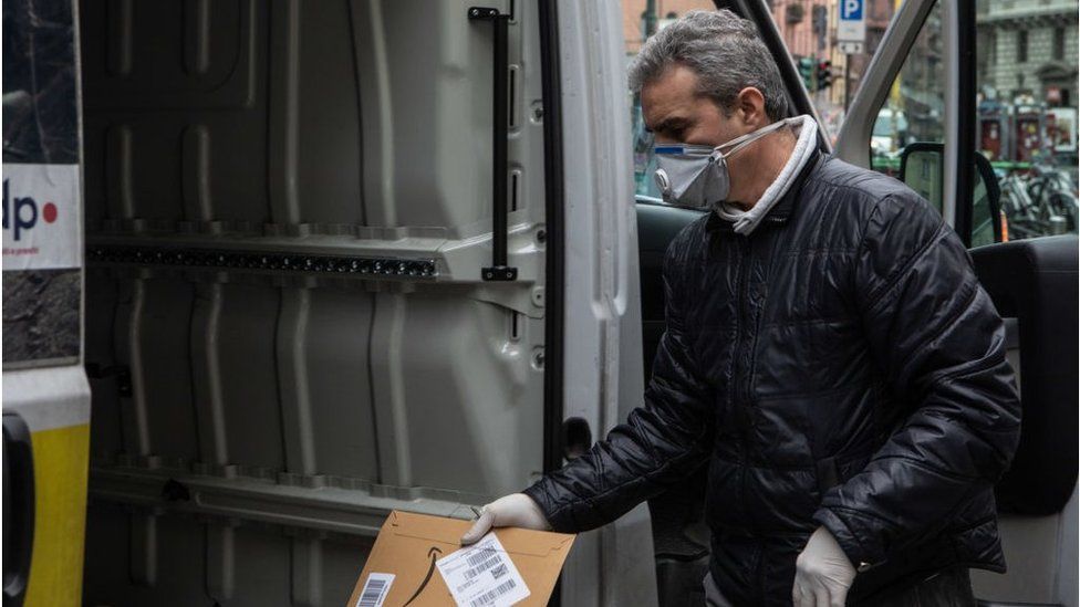 A courier, wearing a respiratory mask, handles an Amazon parcel