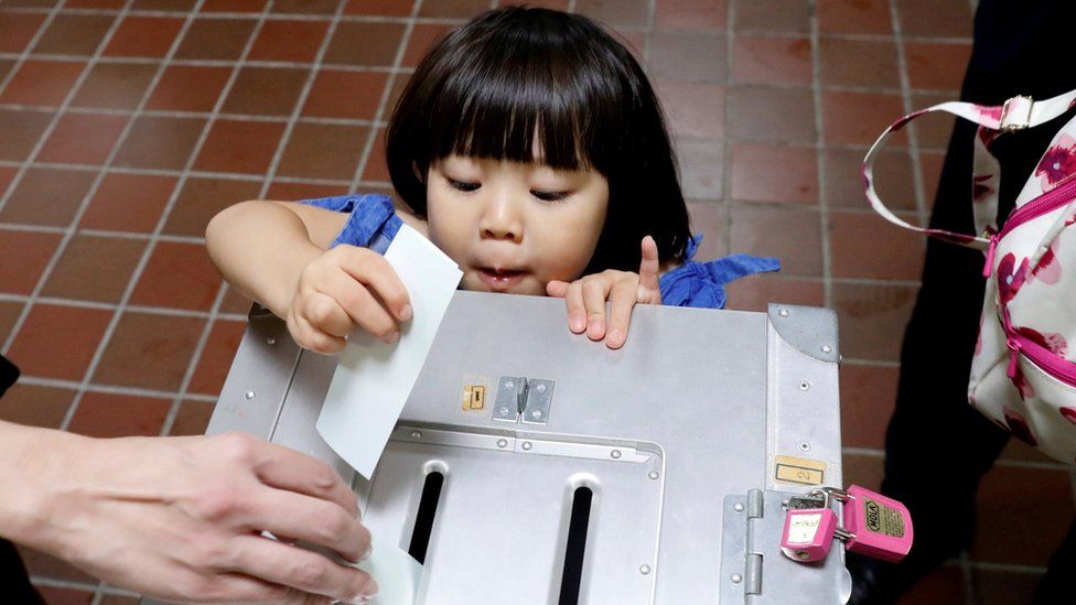A girl casts her father's ballot for a national election at a polling station in Tokyo, Japan October 22, 2017