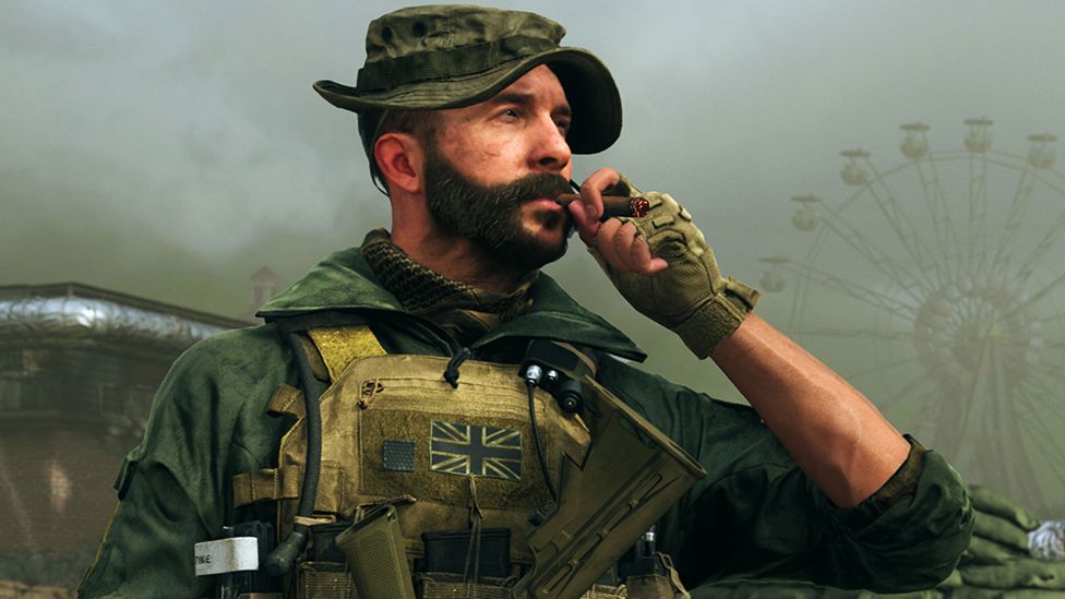 A bearded man in army fatigues stands in a landscape made misty by fog or smoke. In the distance we can just make out a ferris wheel. He's wearing a green camouflage hat with a brim. He's wearing a green camouflage jacket under a tactical vest which has a union flag on the chest. He's holding a cigar to his lips as he surveys the landscape.