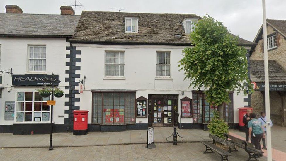 The town's post office with it's red post box and a tree outside.