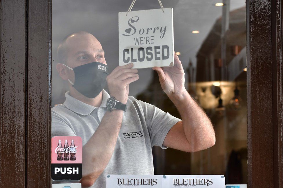 A man puts a "closed" sign in the window of his cafe