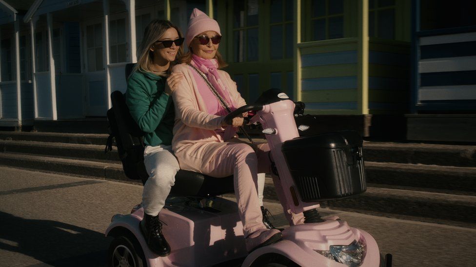 Peg and Chloe riding together on a mobility scooter