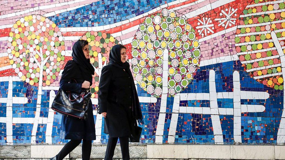 Iranian women walk past mural in Tehran (file photo)