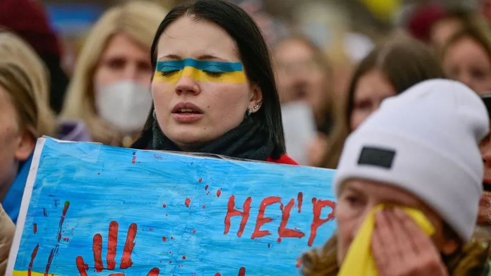A protester with a Ukrainian flag on her face in Berlin holds a placard reading "HELP" in red paint