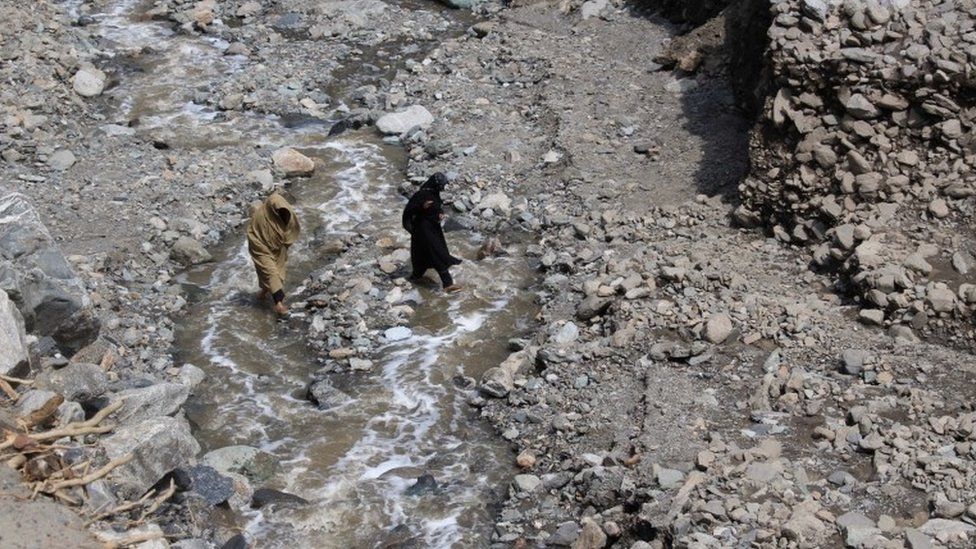 Women cross a stream after the road was destroyed during flash floods in Ursoon, a village near Chitral, on July 3, 2016.
