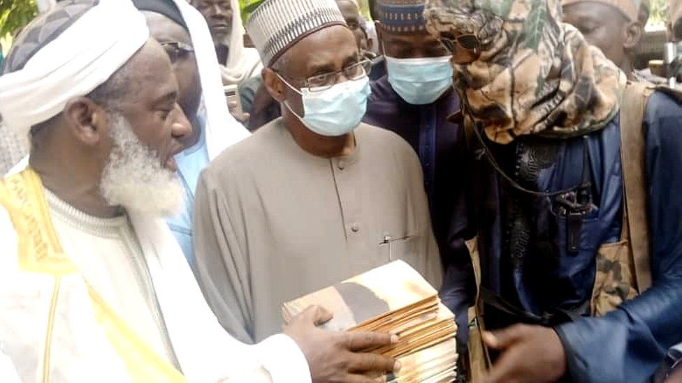 Sheikh Gumi handing a stack of books to a man in hood