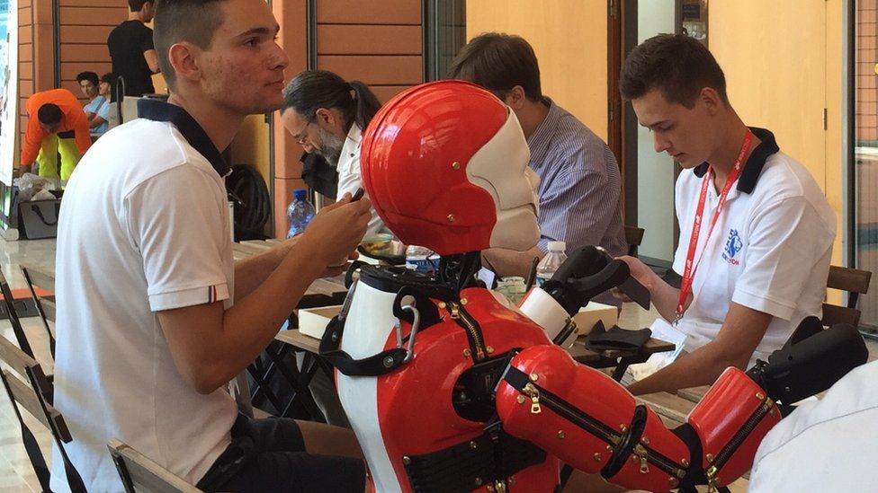 A robot sits at a dining table with human companions