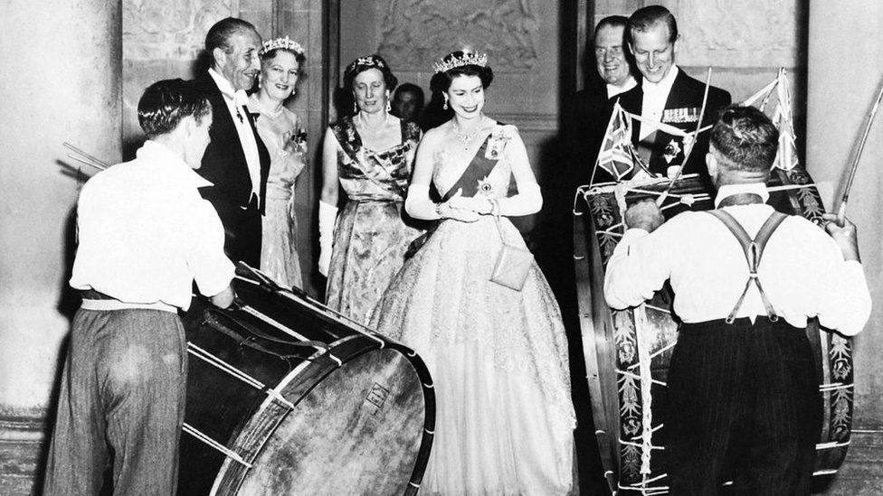 John Warden Brooke, 2nd Viscount Brookeborough (L), Queen Elizabeth II (C) and her husband Prince Philip, Duke of Edinburgh listen to drummers, on July 3, 1953 during their official visit to Northern Ireland
