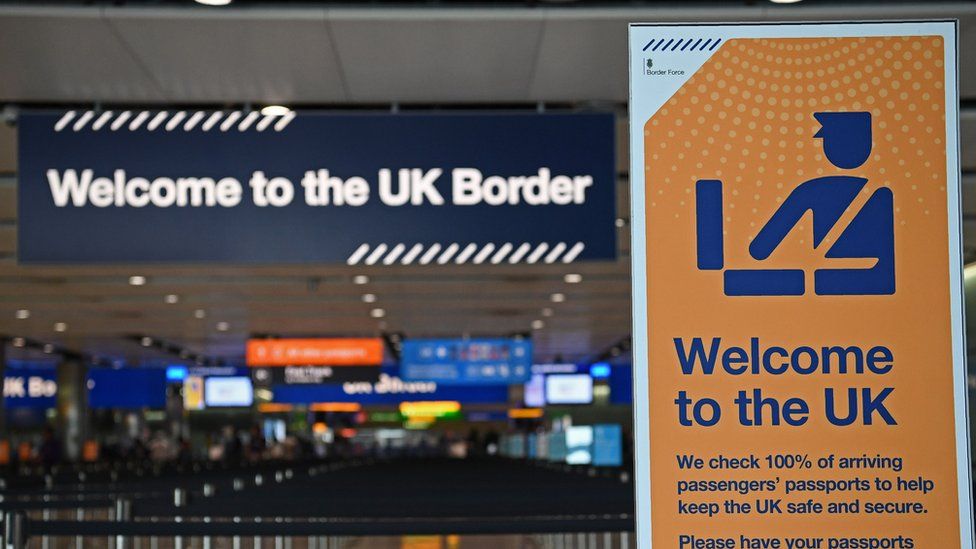 A photo of the UK Border Control at an airport shows two signs, reading "Welcome to the UK border" and "Welcome to the UK", with warning about passport control