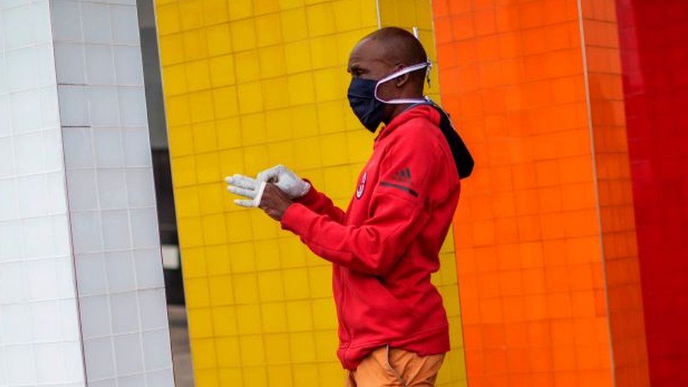 A man wearing a face mask puts on a pair of gloves at the entrance of a shopping mall in Alexandra, Johannesburg, in 2020.