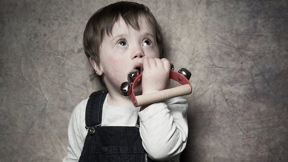 A young boy holds a musical rattle up to his mouth