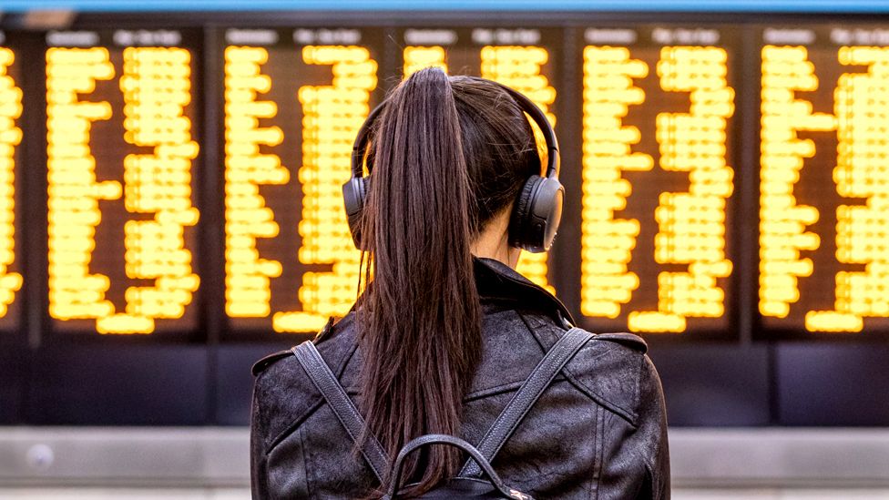 A woman looks at a train times board in a station