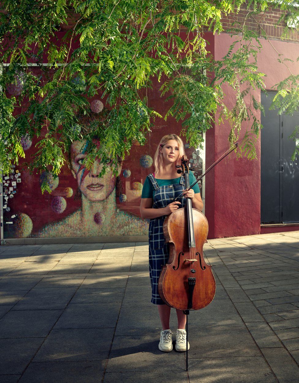 A musician poses with a cello on a street in Brixton, London