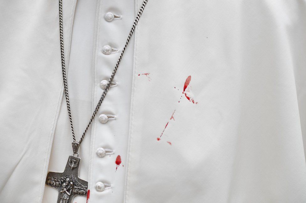 The pope's white tunic is stained with blood.