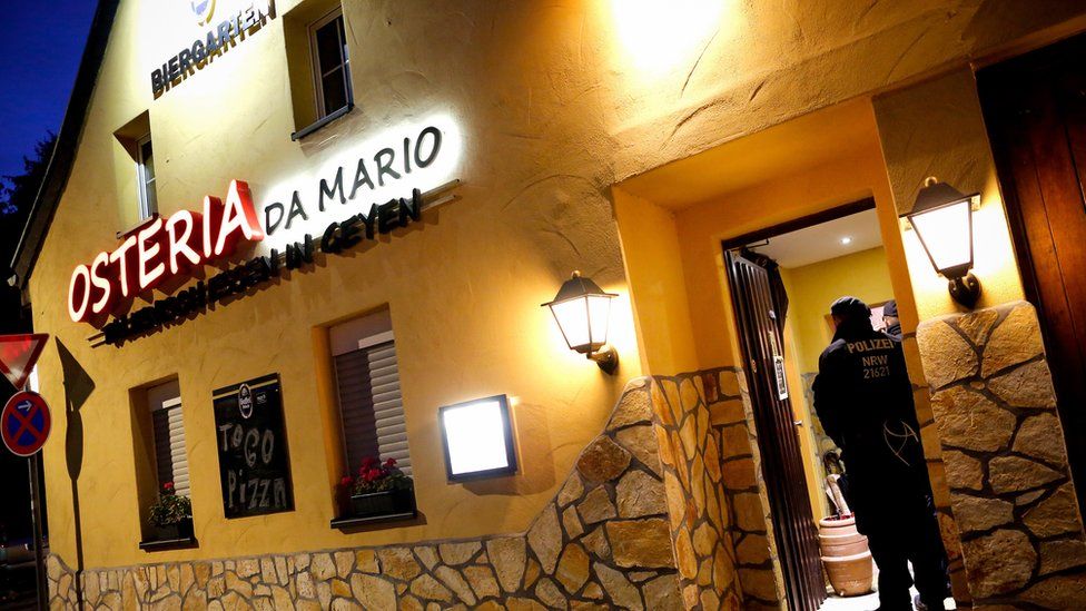A sign on a yellow-painted two-story house declares this Italian restaurant to be Osteria Da Mario - but two police officers guard its open door in this dawn photo