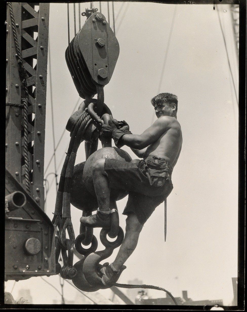A labourer hangs on a connector in the sky.