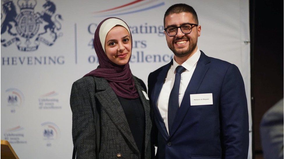 Dr Maisara Al Rayyes and his fiancée pose for a photo in front of a Chevening Scholarships branded backdrop