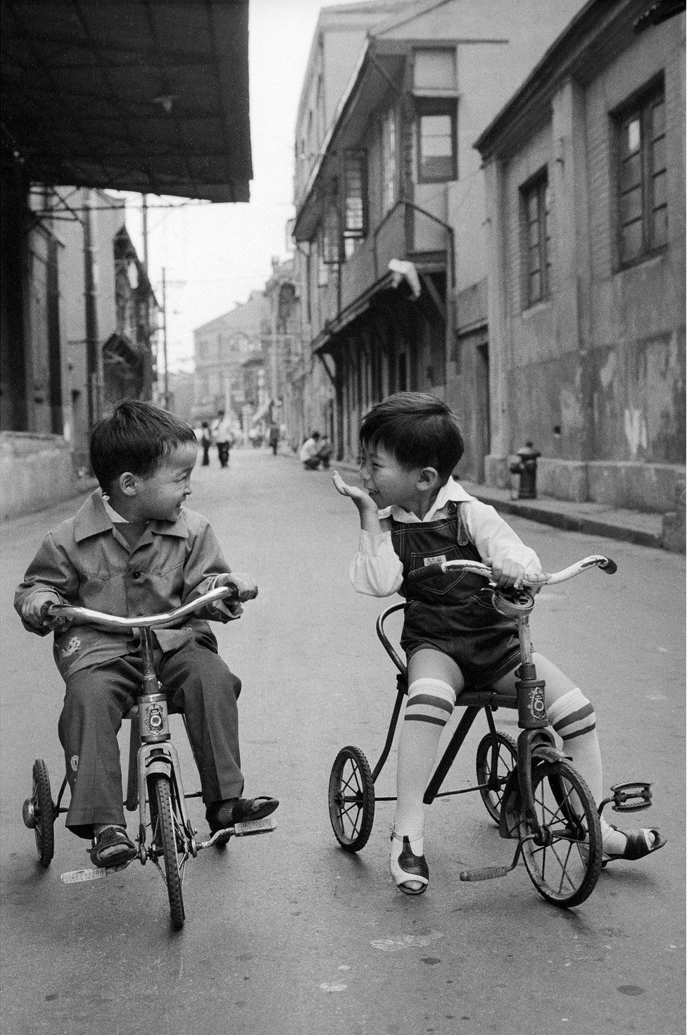 Two boys sit on bikes in the street