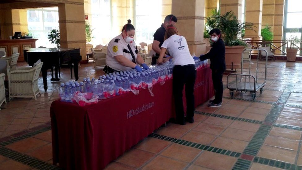 Masked hotel staff prepare water bottles for guests
