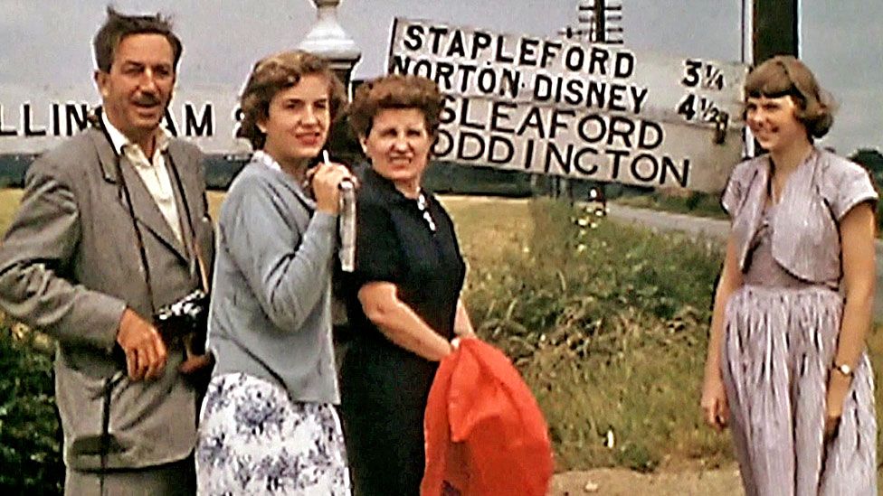 Walt Disney and his family standing by a road sign to Norton Disney