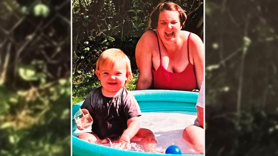 Chloe Fussell as a young child playing in a paddling pool as her mother watches on