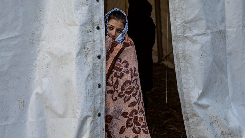 A girl peeking through a tent in a reception centre in Hungary