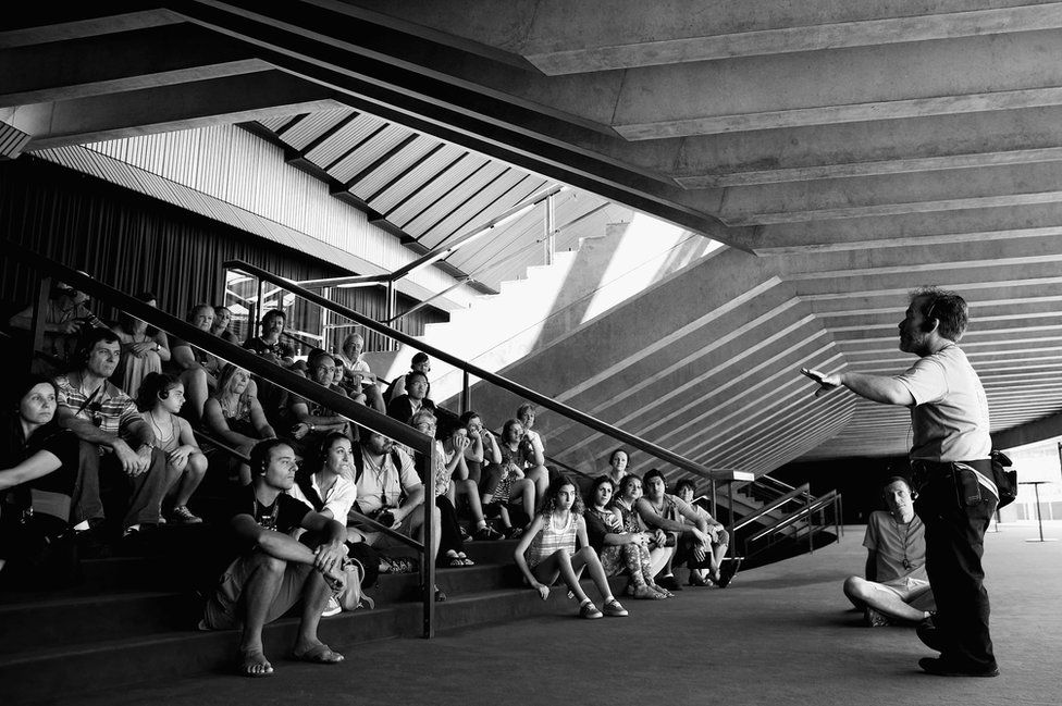 A guide leads a group of tourists around the Sydney Opera House