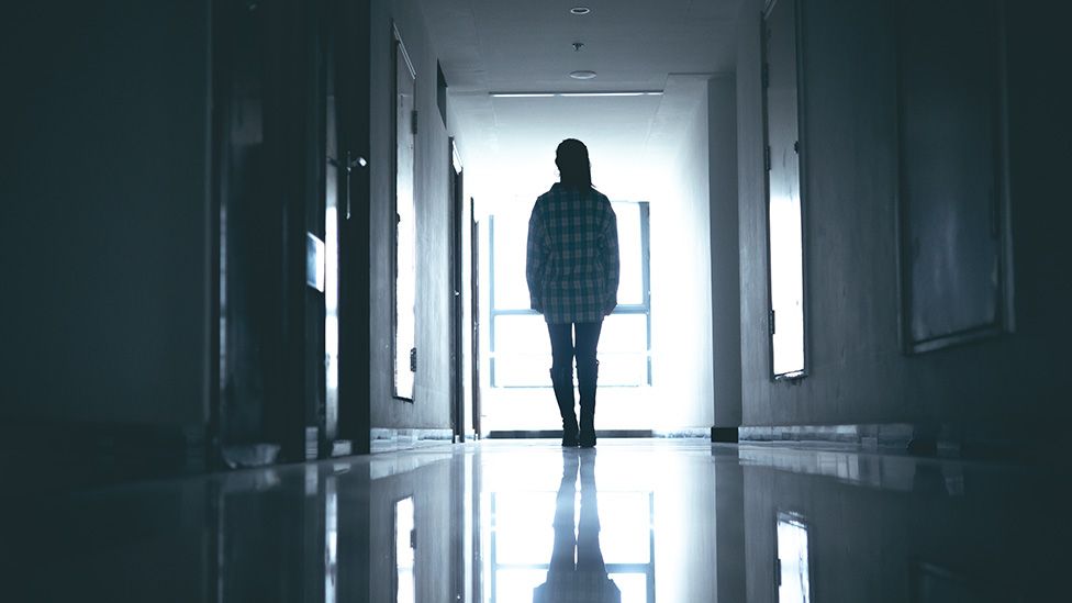 Silhouette of young woman in what looks like a dark hospital ward