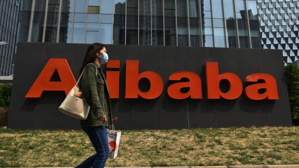 Woman walking past Alibaba sign at company headquarters.