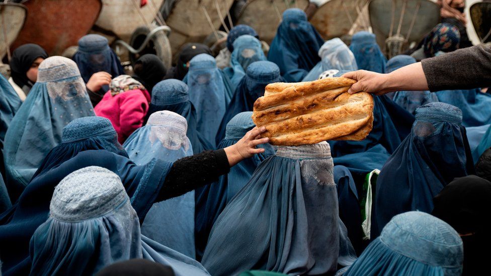 A woman in a burqa reaches out for a loaf of bread. Photo taken in Nov 22