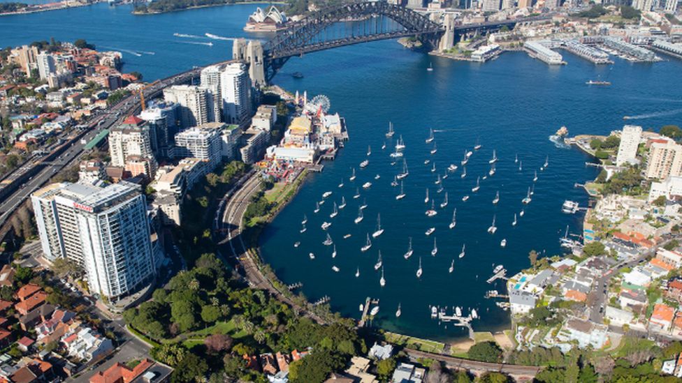Aerial view of Sydney harbour from the north side, with the harbour bridge and a bay full of boats in the foreground