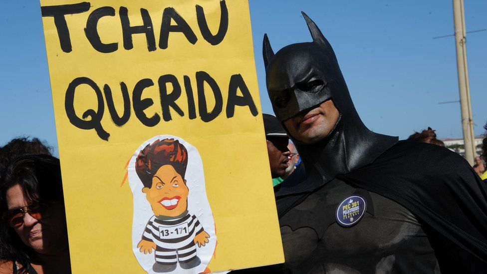 A man dressed as Batman holds up a sign reading "bye darling", referring to President Rousseff