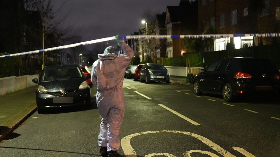 A police officer raises a cordon at a scene following an incident where a woman and children were attacked with a corrosive substance/alkaline, south London