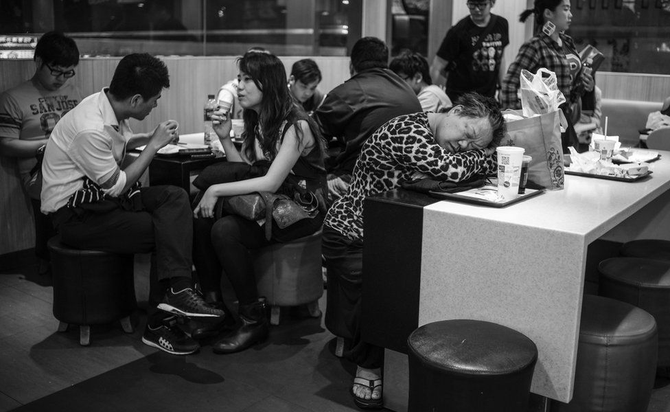 A homeless woman asleep among awake regular customers in the restaurant