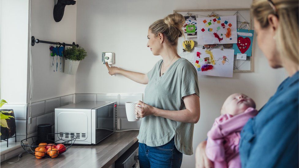 Woman in her kitchen adjusting thermostat