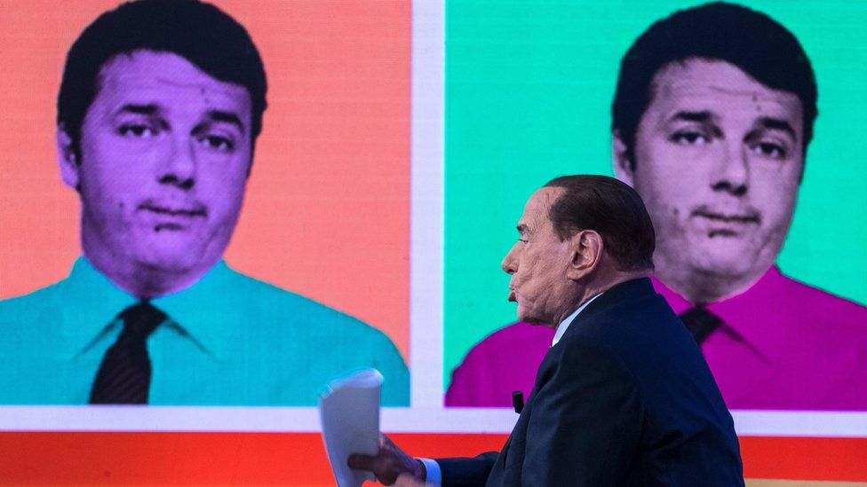 Former Italian prime minister Silvio Berlusconi speaks during a TV studio debate next to the backdrop of the former Italian prime minister Matteo Renzi