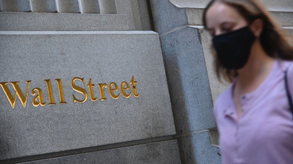 woman in mask walks by Wall Street sign